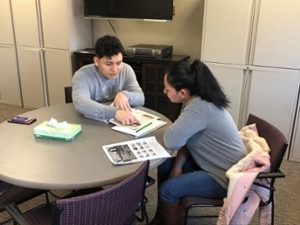 Language Center tutor showing a student something on papers at a round table at the Language Learning Center.