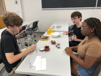 3 Students serving tea while sitting at table