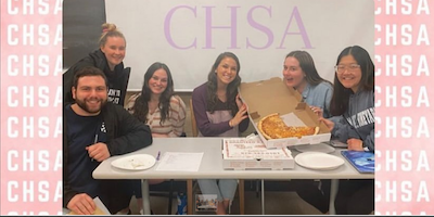 Five female members and one male member of the Counseling and Human Services Association at the University of Scranton sit at a table during a student club fair. 