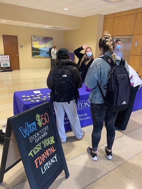 A student stands behind a table handing out information to a group of university students
