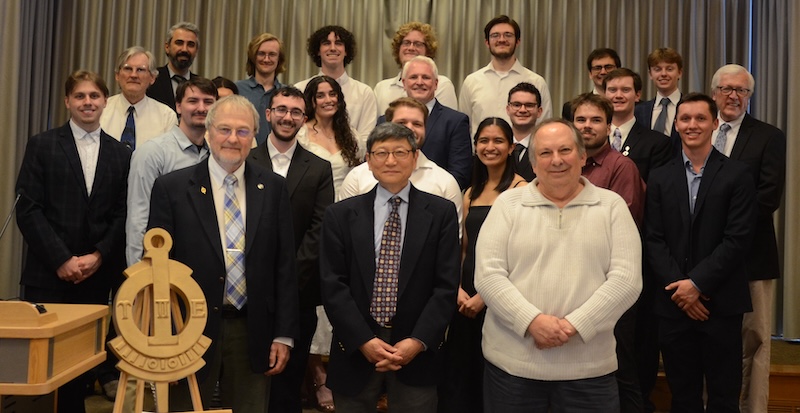 Seventeen college students stand with seven professors for a group photo.