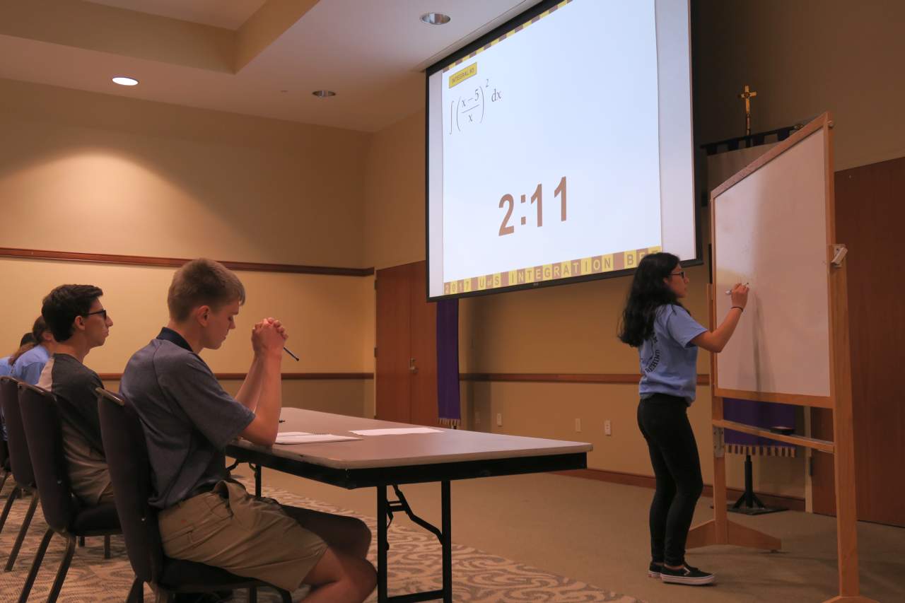 A female student integrating a rational function at the whiteboard in front of the class during the 2017 Integration Bee