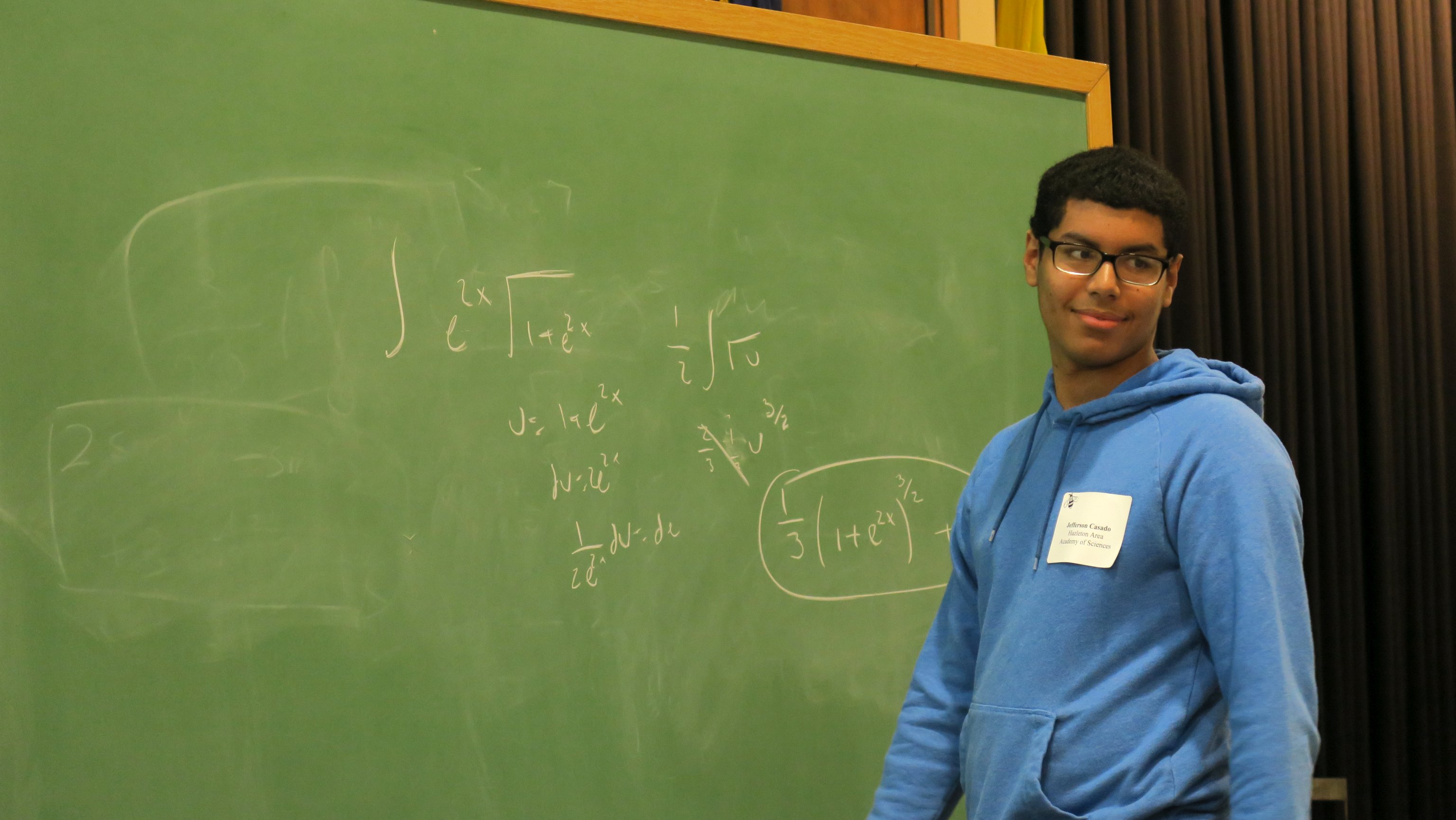 A Hazelton Area Academy of Sciences male student solving an exponential integral by substitution at the blackboard during the 2019 Integration Bee
