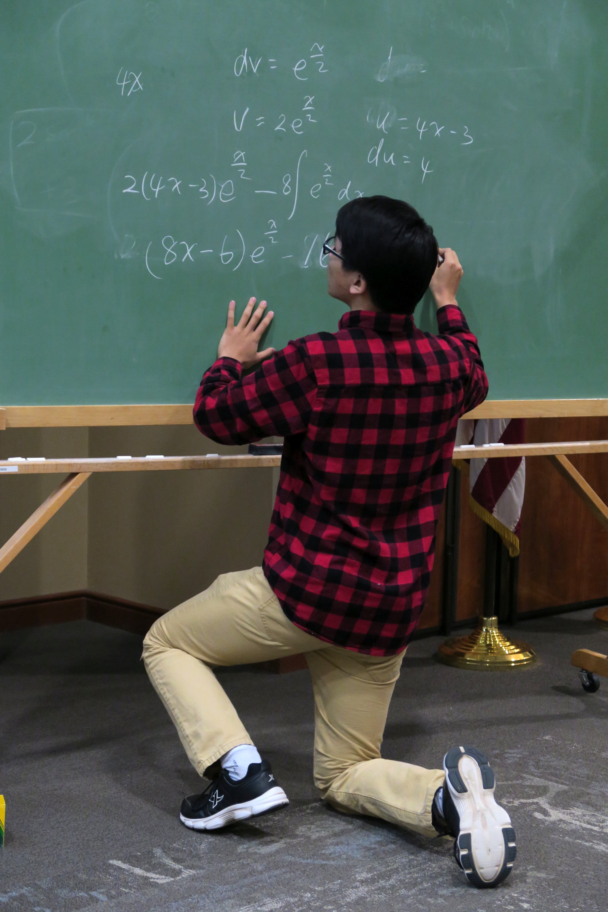 A male student solving an exponential integral by parts at the blackboard during the 2019 Integration Bee
