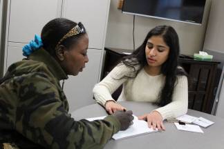 LLC tutor and community member writing on notebook pages together on round table at Language Center.