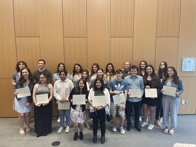 20 students standing while holding their Alpha Mu Gamma certificates.