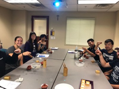 Group of students holding up their teacups while gathered at a table