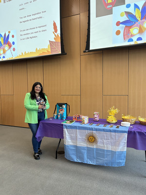 Argentinean FLTA Sheila Mignolet standing in front of a table with the Argentina flag holding mate at her event on "Fall Folktales from Argentina."