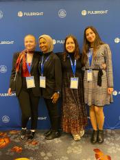 Audrey Seeger, Badoor Albuloushi, Celine Seeger, and Magali Ferrer at the Fulbright Conference wearing nametags and standing in front of a Fulbright backdrop.