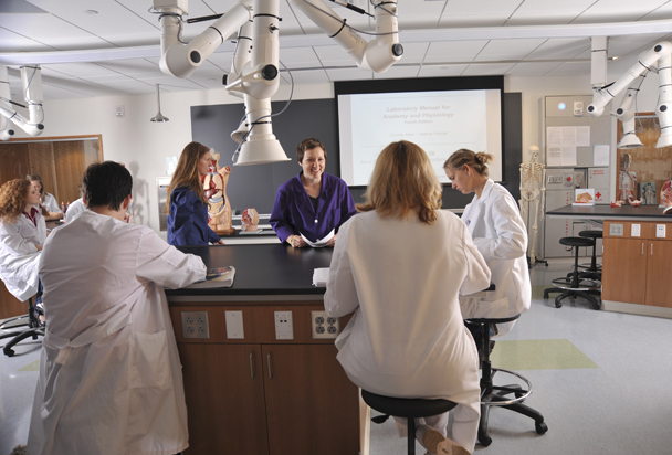 Students wearing white lab coats interacting in the lab setting.
