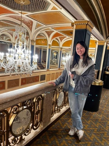 A girl standing on a balcony beside a chandelier 