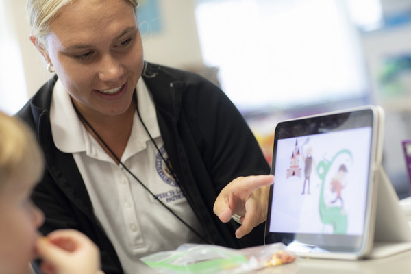 A woman points to a picture on a laptop as a child watches.