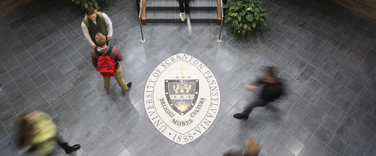 Students walk around the University Seal on the first floor of Brennan Hall.