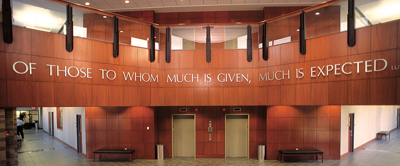Zoomed in view of quote, "Of those whom much is given, much is expected" at the entrance of Brennan Hall
