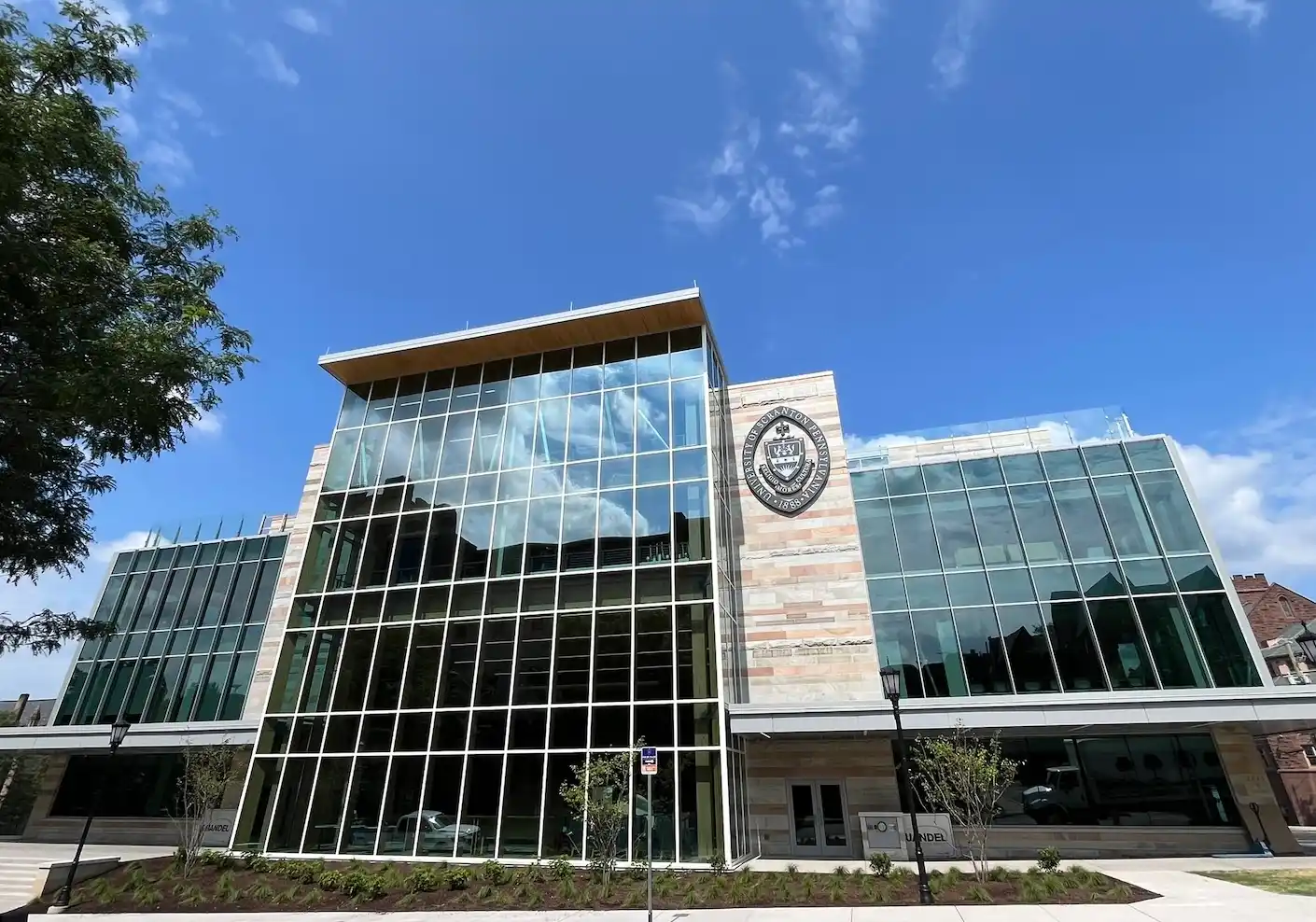 A tan stone academic building with large windows covering the front and a university seal near the top